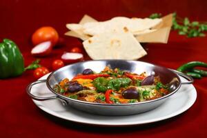 Spicy Shakshuka or Ojja merguez include poached egg, eggplant, capsicum, tomato, red and green chilli pepper served in pan dish isolated on red background side view of arabic food photo