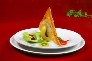 Crispy and Spicy Samosa filled with vegetable and meat with salad served in plate isolated on red background side view of ramadan food photo