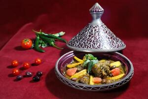 Traditional Moroccan Lamb Tagine served in pot isolated on red background side view of arabic food photo