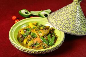 Traditional Moroccan Chicken Tagine served in pot isolated on red background side view of arabic food photo