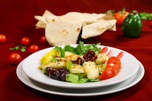 Grilled Halloumi Cheese Salad with grilled cheese, fresh vegetables, olives, tomato, lettuce, lemon and mint served in plate isolated on red background side view of arabic food photo