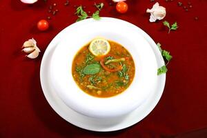 Traditional Moroccan Hrira Soup with lentils, chickpeas, and a medley of vegetables topping with coriander and lemon slice served in bowl isolated on red background top view of arabic food photo
