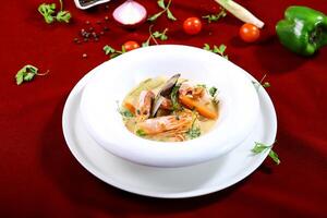 Spicy Tom Yum Soup with Shrimp, creamy coconut milk, cucumber and carrot served in bowl isolated on red background side view of arabic food photo