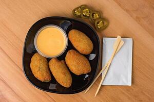 Crispy Jalapeno Poppers with Dipping Sauce served in plate isolated on wooden table top view fast food snacks photo