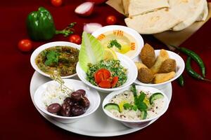 Mix Mezze Platter with Fresh Ingredients mezzeh hummus, Tabouleh Salad, falafel, tabouleh, baba ganoush, lemon, mutabal served with fresh pita bread on red background side view of arabic food photo