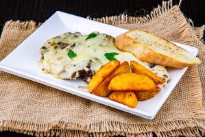 Chicken Steak with Mushroom Sauce, Potato Wedges, and Garlic Bread served on tray isolated on napkin side view of fast food snacks photo