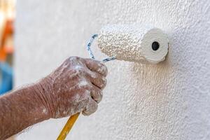 Painters hand using a roller brush to apply white paint to a wall photo