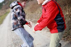 Two young boys playfully engaging in a friendly tussle on a dirt path surrounded by dry grass and trees during a sunny day photo