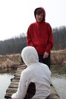 Two boys engaging on a wooden bridge over water in a countryside setting during early spring with a forest backdrop photo