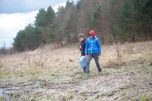Two boys exploring a grassy area near a small pond in the woods during a cloudy day photo