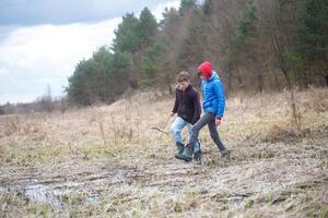 Two children explore a muddy field in early spring, collecting sticks and enjoying nature's beauty together photo
