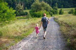 A child and adult enjoy a peaceful walk together on a gravel path through lush greenery in the serene countryside during late afternoon photo