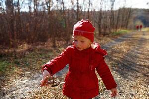 A child in a red coat exploring a wooded path on a sunny day, discovering nature and enjoying outdoor adventures photo
