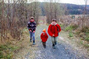 Three children in bright jackets run along a forest path on a cool autumn day surrounded by trees and nature photo