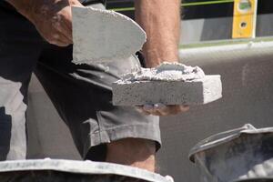 close up of the hands of a bricklayer applying cement mortar to a brick to stick it into the masonry for building a house, High quality photo