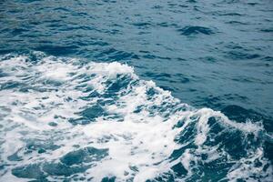 Wave on blue water and white foam on the tops of the waves from under the side of a floating boat, space for text photo