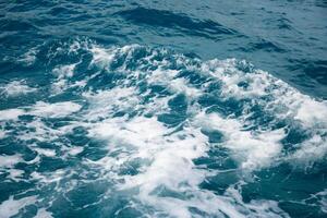Wave on blue water and white foam on the tops of the waves from under the side of a floating boat, space for text photo