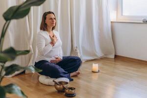 A woman sits on the floor with her eyes closed, practicing deep breathing exercises. She inhales and exhales slowly photo