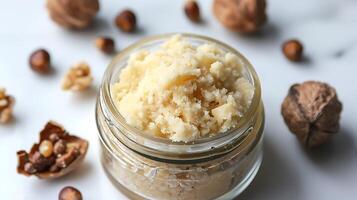 luxurious shea butter face scrub in a glass jar surrounded by shea nuts on a clean white backdrop. photo