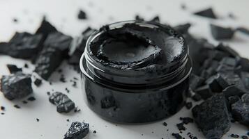 activated charcoal face mask in a jar on a plain white background with charcoal pieces. photo