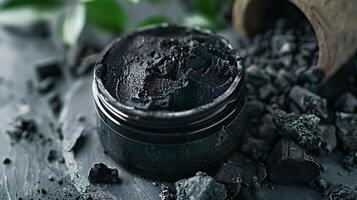 activated charcoal facial scrub container with charcoal pieces on tabletop in bright room setting photo