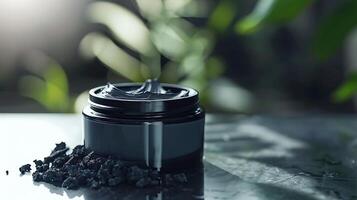 activated charcoal facial cream container next to activated charcoal pieces on table photo