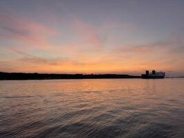 A ship sails from the port into the sea at sunset, casting a warm glow on the tranquil waters. photo