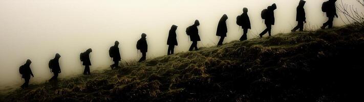 A group of hikers' silhouettes climb a grassy hill in a foggy landscape, captured from a low-angle side view in an ultra-wide shot photo