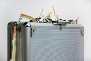 A silver briefcase overflowing with bills sits on a white background photo