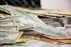 A stack of US dollar bills with a hundred dollar bill on top, resting on a silver case photo