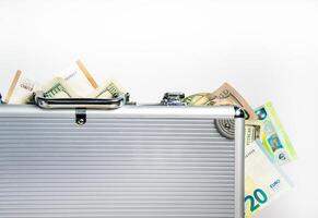 A silver briefcase, partially open, with US dollar bills and euro bills spilling out photo