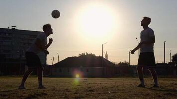 Silhouette of professional footballers kicking soccer ball with their heads on stadium at sunset. Two sportsmen showing tricks with ball while passing it to each other at field. Freestyle football photo