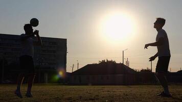 Silhouette of professional footballers kicking soccer ball with their heads on stadium at sunset. Two sportsmen showing tricks with ball while passing it to each other at field. Freestyle football photo