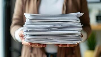 A person stands indoors, carefully balancing a tall stack of papers, ready to tackle work tasks amid a cozy, sunlit workspace adorned with plants and office supplies photo