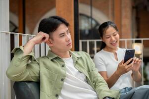 A man is sitting on a couch in a cafe with a moody expression, feeling ignored by his girlfriend. photo