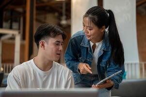 Two Asian friends or colleagues are in a coffee shop, discussing a project while working together. photo