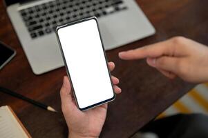 A top view of a man holding a smartphone with a white screen mockup above a desk. photo