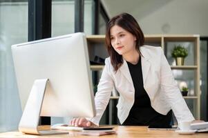A businesswoman is standing at her desk, typing on a computer keyboard and looking at the screen. photo