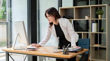 A businesswoman is standing at her desk, typing on a computer keyboard and looking at the screen. photo