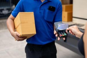 A customer tapping her credit card on a card reader before receiving a package from a delivery man. photo