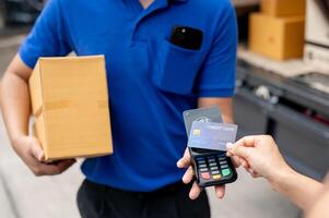 A customer tapping her credit card on a card reader before receiving a package from a delivery man. photo
