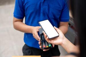 A customer tapping her smartphone on a card reader before receiving a package from a delivery man. photo