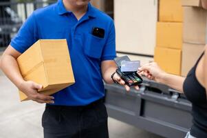 A customer tapping her credit card on a card reader before receiving a package from a delivery man. photo