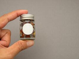 Hand holding of a bottle container herbal with a blank label over a gray background photo