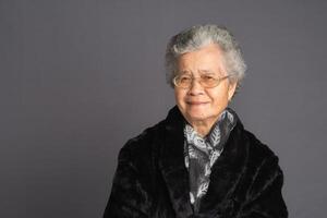 Senior Asian woman in a sweater and scarf looking at the camera with a smile while standing on a gray background photo