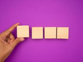 Hand holding a blank wooden cube and three arranged in a row over a purple background photo