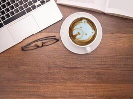 Top view of a laptop, a book, glasses, and a coffee cup on a wooden table photo