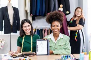 Young two fashion designers use digital tablet meeting with graphic designer discuss show sample dress design new collection on screen on desk while working in sewing workshop photo