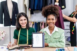 Young two fashion designers use digital tablet meeting with graphic designer discuss show sample dress design new collection on screen on desk while working in sewing workshop photo