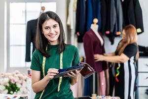 Smiling Caucasian female fashion designer works in studio choosing colorful fabric for a dress design collection and looking at camera , choose clothing colors for tailoring and designing photo